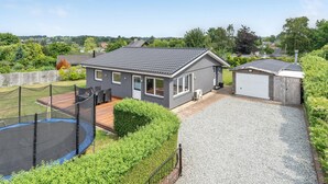 A modern house with a grey exterior, a wooden deck, a trampoline, and a gravel driveway. - Amazing home in Frederiksværk with WiFi (Frederiksværk)