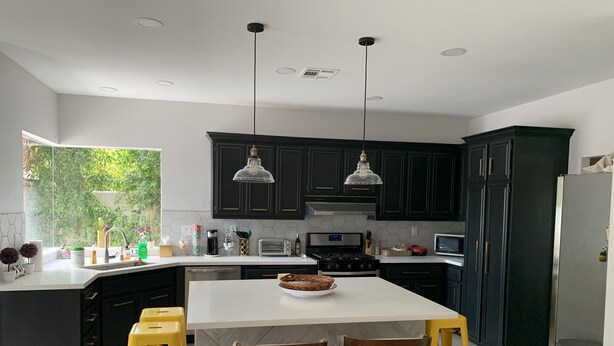 Una cocina moderna con armarios oscuros, una isla blanca, taburetes amarillos e iluminación colgante.