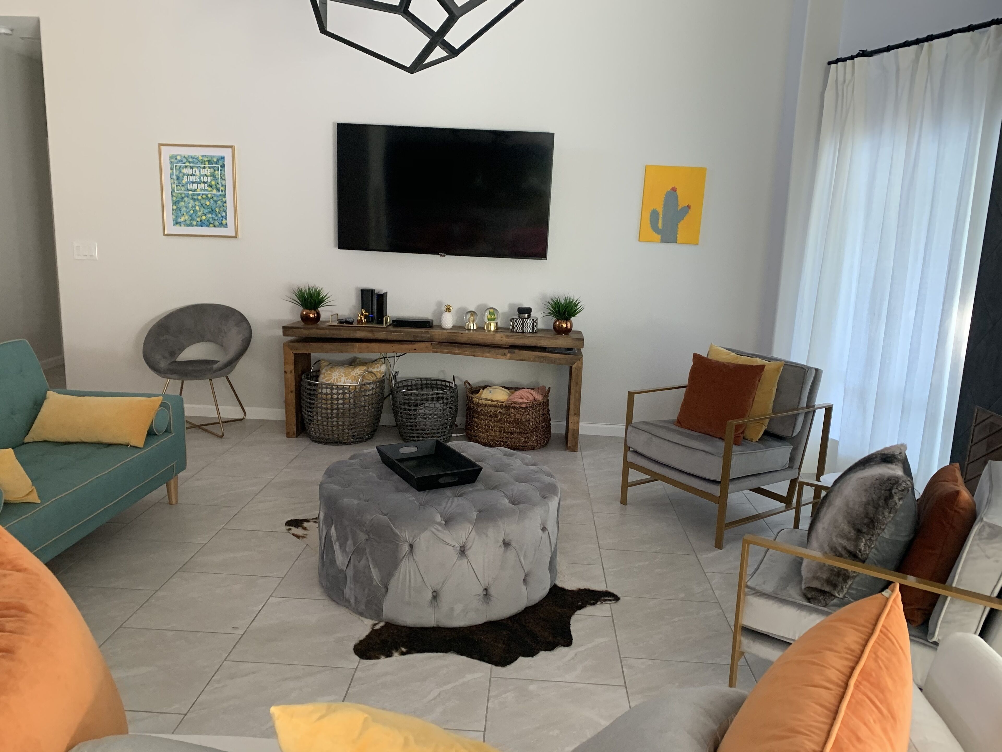Un salon moderne avec un téléviseur à écran plat, une console en bois, un canapé gris, un fauteuil gris et un pouf capitonné.