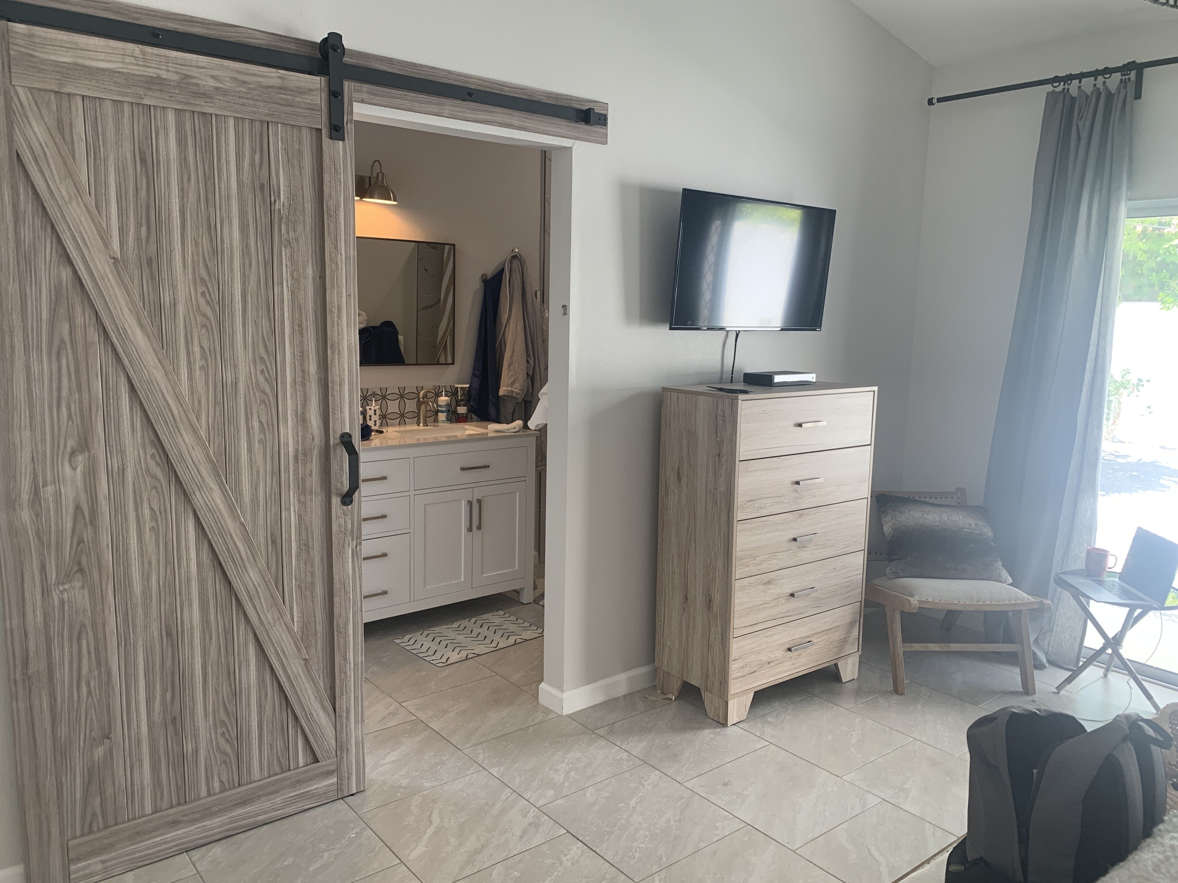 Ein Zimmer mit einer Schiebetür zu einem Badezimmer, einer Holzkombination mit Fernseher darauf, einem Stuhl und einem Rucksack auf dem Boden.