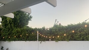 Un área de piscina moderna al aire libre con un jacuzzi, rodeada por un muro blanco y vegetación.