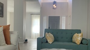 Una sala moderna con un pouf gris capitonado, un sofá turquesa con almohadones decorativos y un sillón blanco.