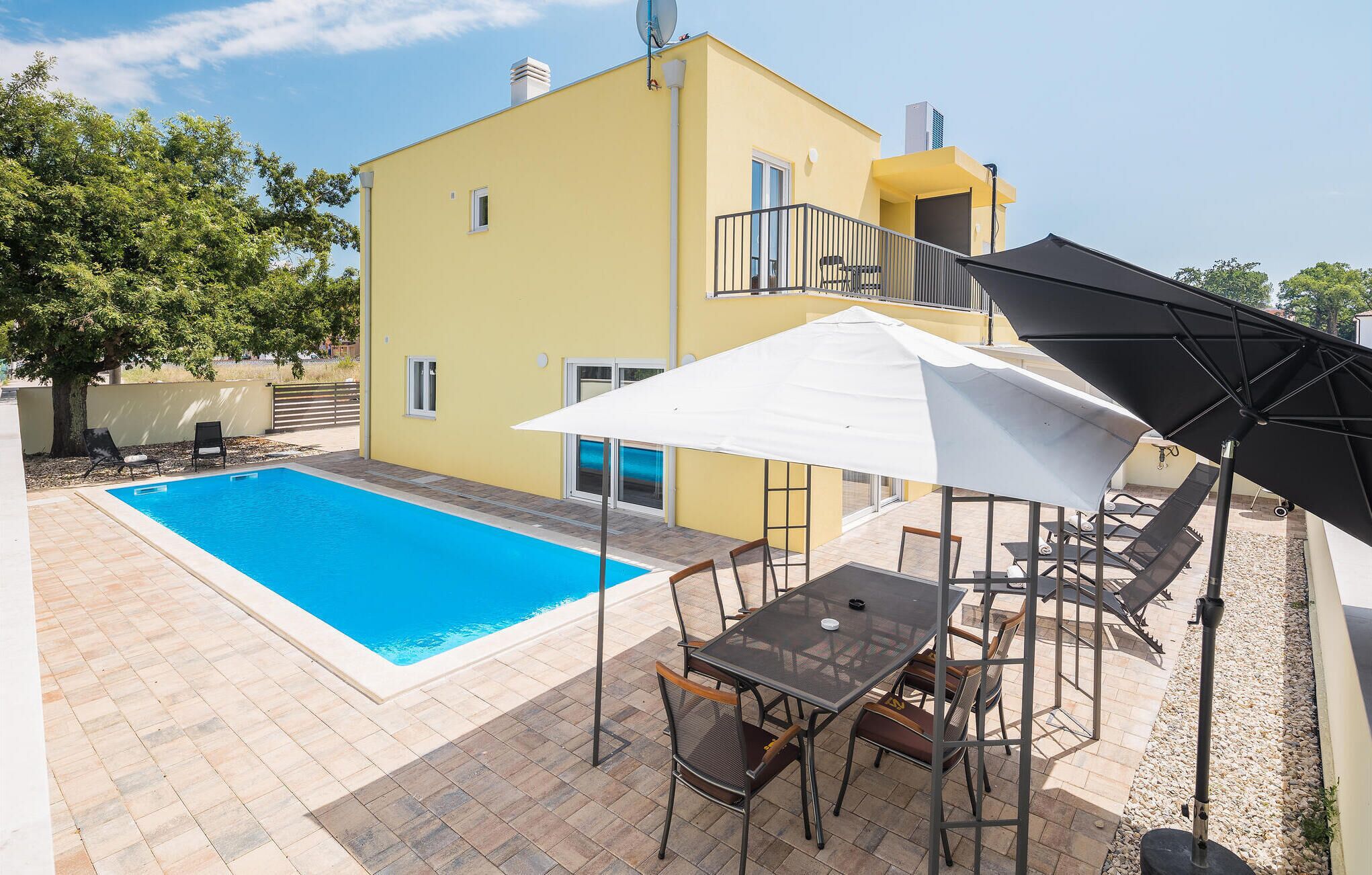 A yellow building with a swimming pool, outdoor seating, and a covered patio area.