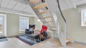 A spacious living room with a wooden staircase, a gray armchair, a red chair, and a small table.