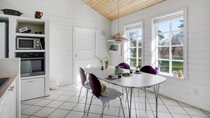 Een moderne keuken met witte kasten, een inbouwoven, magnetron en een eethoek met een ronde tafel en stoelen.