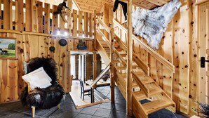 Un interior rústico de madera con una escalera, un sillón cubierto de pieles y un adorno de piel colgado.