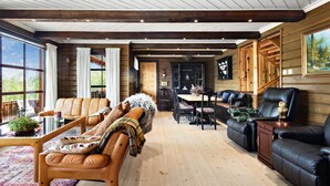 Una sala de estar amplia con techo de madera, ventanas grandes y una chimenea acogedora.