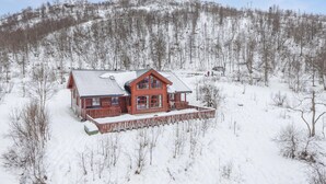 Una cabaña de madera con un amplio porche, rodeada por un bosque nevado.