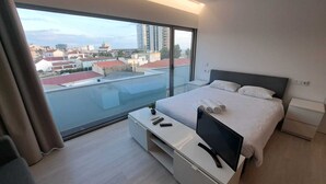 A modern hotel room with a large balcony, a bed with neatly folded towels, a TV, and a small table. - Figueira Beach Apartment (Buarcos)