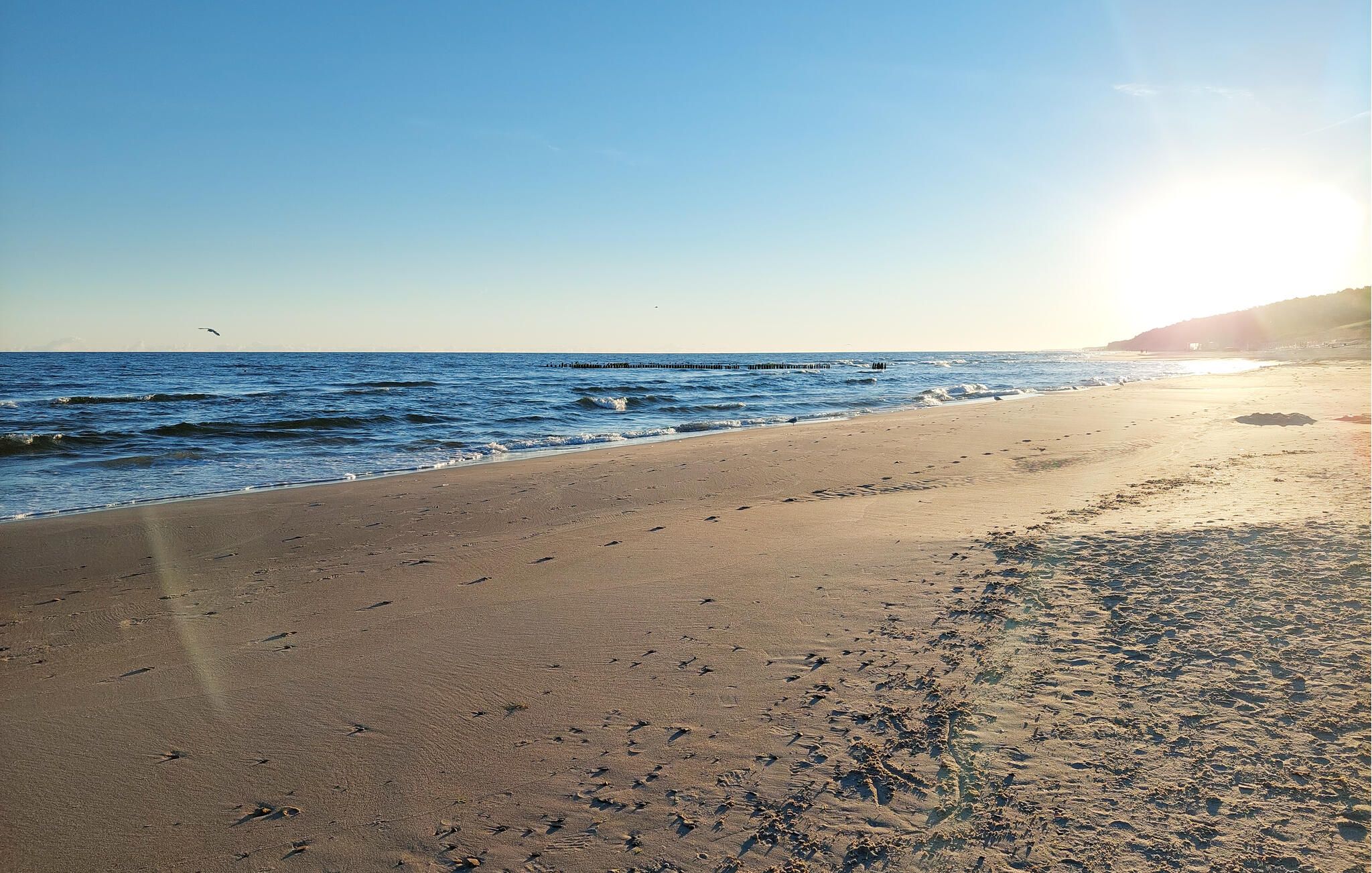 A beach with footprints, a pier, and a clear sky.