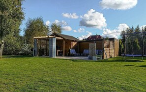 Une cabane en bois avec une véranda, un espace salon extérieur et un trampoline.