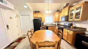 A kitchen with wooden cabinets, a black refrigerator, a dining table with chairs, and a microwave above the stove. - Greater Zion Villa at Sports Village (St. George)