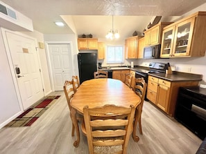 A kitchen with wooden cabinets, a black refrigerator, a dining table with chairs, and a microwave above the stove.