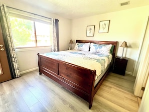 A bedroom with a wooden bed, two bedside tables, a window with curtains, and two wall-mounted pictures.