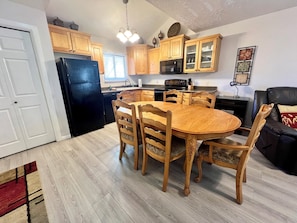 A kitchen with wooden cabinets, a black refrigerator, a dining table with chairs, and a black sofa.