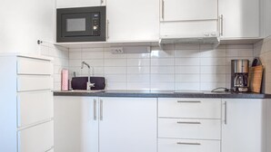 Una cocina con gabinetes blancos, un microondas, una estufa y una cafetera.