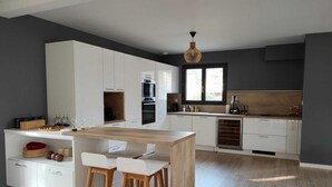 A modern kitchen with white cabinetry, a wooden island with bar stools, and a large window providing natural light. - Pleasant Villa Domaine du Golf Heated swimming pool (Biscarrosse)