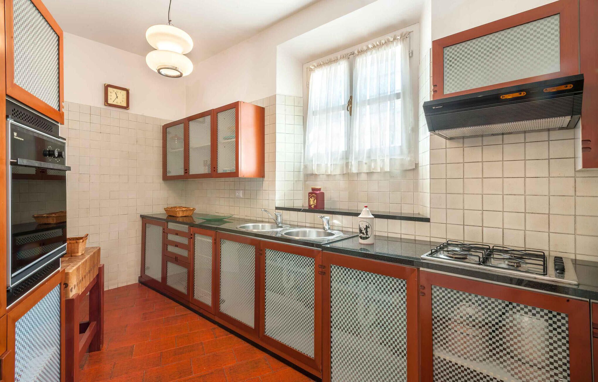 A kitchen with wooden cabinets, a gas stove, a sink, and a window with curtains.