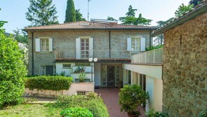 Un bâtiment en pierre de deux étages, avec un toit en tuiles, un balcon doté d’une balustrade en métal et une cour intérieure agrémentée de plantes en pot.