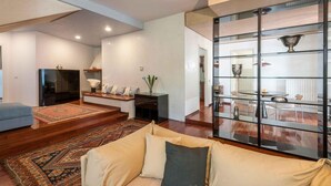 Un salon moderne comprenant un canapé, une table basse, un téléviseur et une cloison en verre avec des étagères.