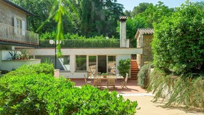 Une maison à deux étages dotée d’un balcon, d’un coin repas avec mobilier d’extérieur et entourée d’une végétation luxuriante.