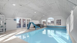 Une piscine intérieure avec un toboggan bleu, de grandes fenêtres et un plafond haut.