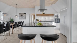 Une cuisine moderne dotée d’un îlot central, d’appareils électroménagers en acier inoxydable et d’un coin repas avec des chaises et une table noires.