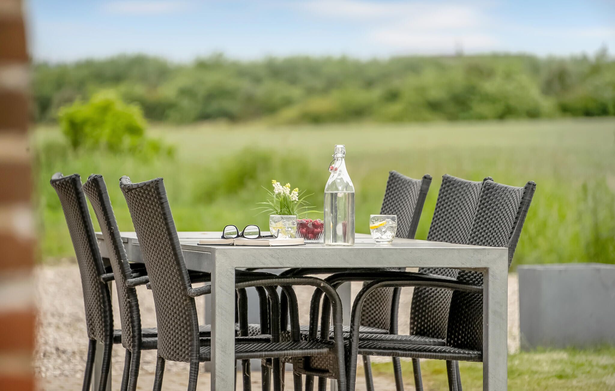 A table set outdoors with wicker chairs, a bottle, glasses, and a small plant.