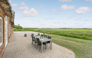 A patio with a table and chairs, a thatched-roof building, and a view of a green field.