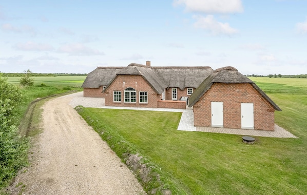 A brick building with a thatched roof, a gravel driveway, and a grassy field in the background.