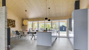 Ett modernt kök med stora fönster, en matplats med stolar och utsikt över omgivningen.