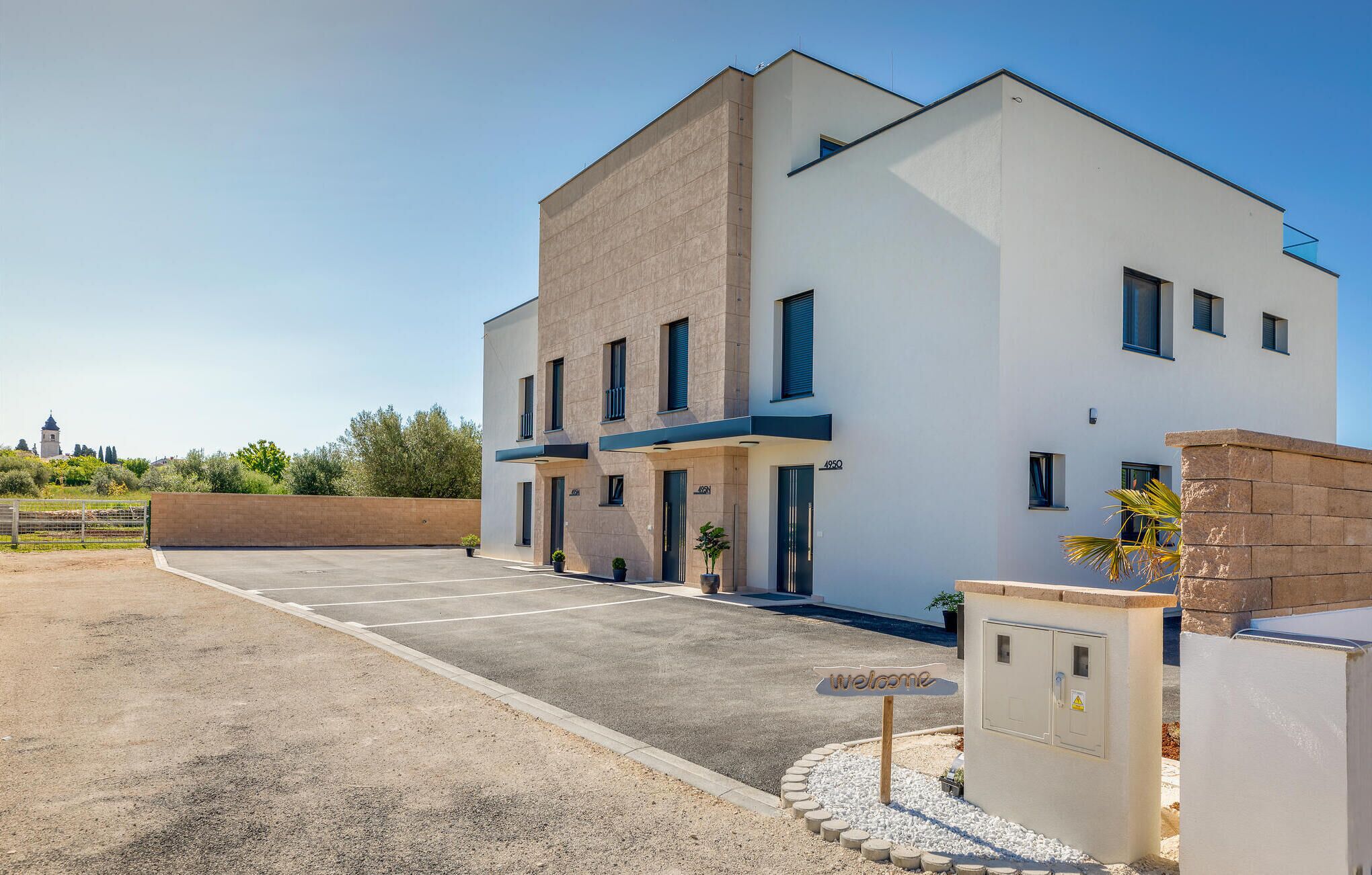 A modern two-story building with a flat roof, a parking lot, and a small garden area with a welcome sign.