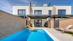 Un edificio residencial moderno con piscina, mobiliario de exterior y zona de barbacoa.