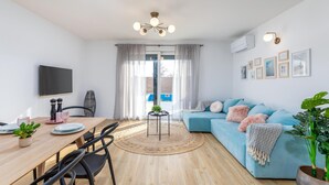 Una sala de estar moderna con un sofá azul, una mesa de comedor de madera y un televisor montado en la pared.
