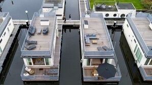 A modern floating house with multiple decks, outdoor seating areas, and a central water feature.