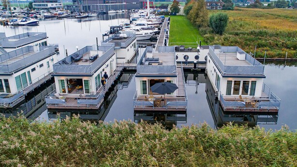 A marina with multiple floating homes connected by walkways, featuring outdoor seating areas and a view of the water.