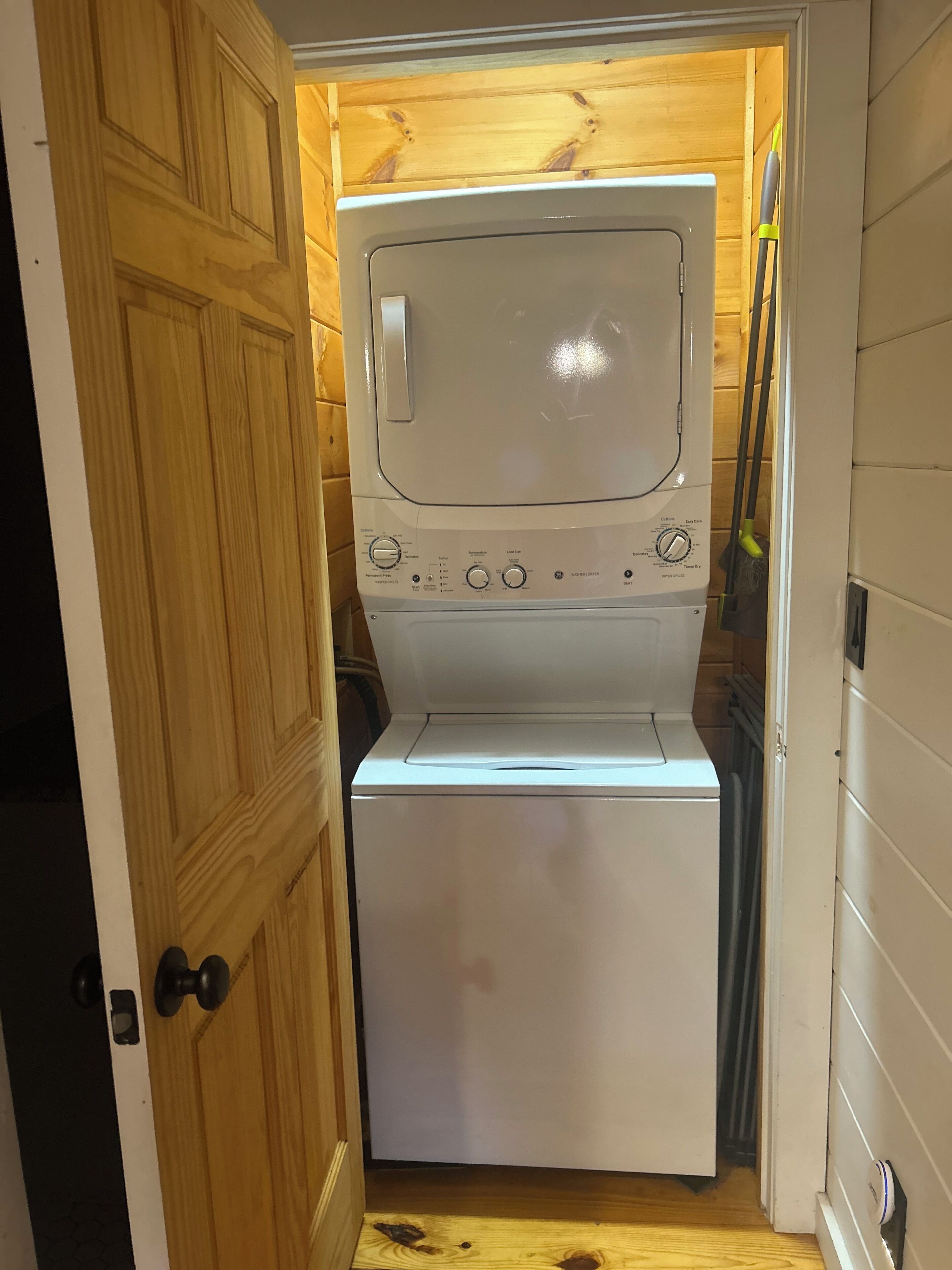 Une petite buanderie équipée d’un lave-linge et d’un sèche-linge intégrés, avec des murs en bois et une porte.