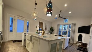 A spacious kitchen with a large island, white cabinetry, and a modern pendant light fixture.