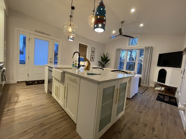 A spacious kitchen with a large island, white cabinetry, and a modern pendant light fixture. - Custom cottage close to everything-Enjoy long walks on beach without the crowds! (Westerly)
