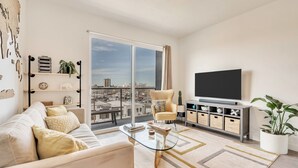 Un salón moderno con sofá, mesa de centro, televisor y un balcón con vistas a la ciudad.