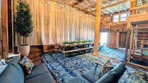 Un interior rústico con techo de madera, luces colgantes, una gran maceta con árbol, un sofá y una mesa de picnic.