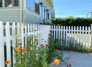 Stroll through a charming garden surrounded by a picket fence and a house with a welcoming front porch.