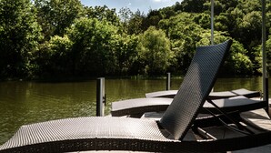 Een steiger met ligstoelen met uitzicht op een meer, omringd door weelderige begroeiing.