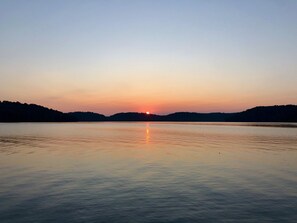 Un lago tranquilo al atardecer con la silueta de colinas al fondo.