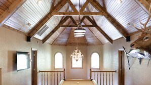 Een ruime kamer met een pooltafel, houten balken in het plafond, een kroonluchter en een opgezette hertenkop.