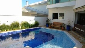 A modern pool area with a curved design, surrounded by potted plants and a wooden bench. - Beautiful house in Peruibe (SP)