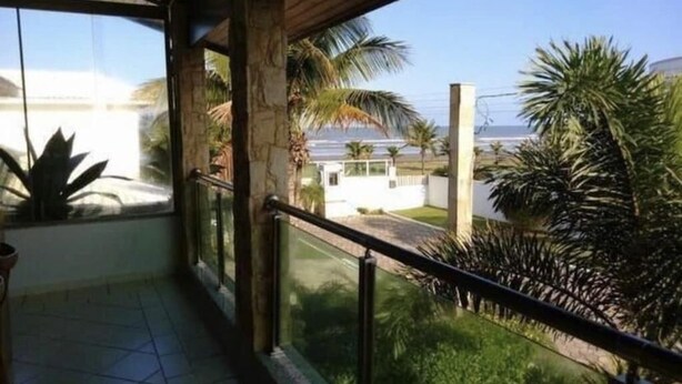 A balcony with a view of a residential area, including palm trees and a white building. - Beautiful house in Peruibe (SP)