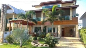 A two-story house with a covered patio, a stone facade, and a well-maintained garden with palm trees and shrubs. - Beautiful house in Peruibe (SP)