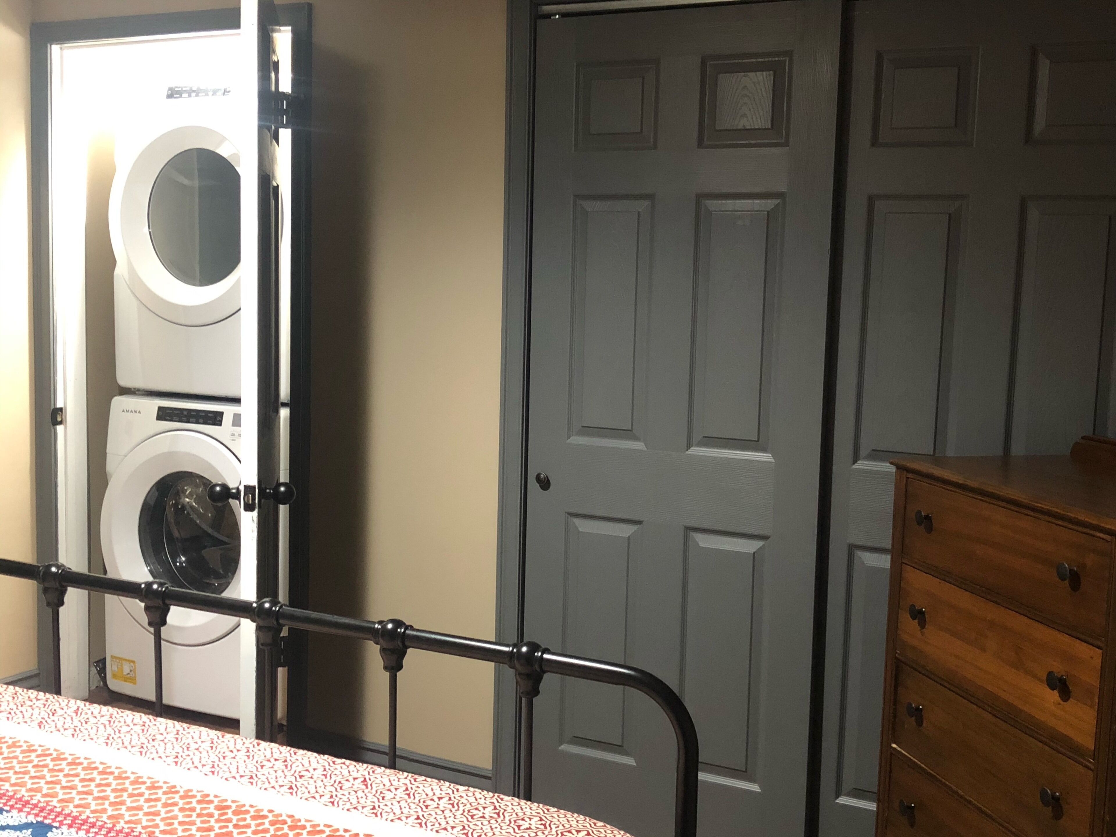 Een wasserette met gestapelde wasmachines en drogers, een grijze deur en een houten dressoir.
