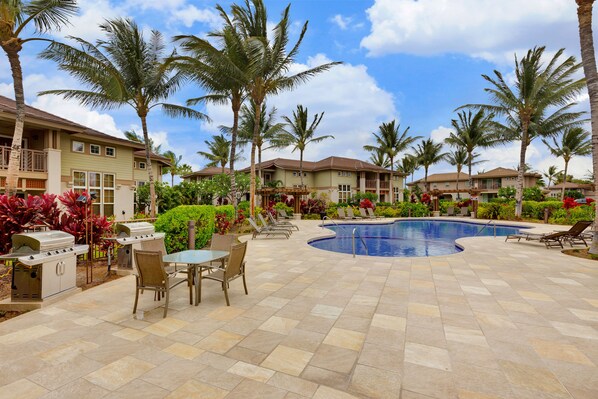 A resort with a swimming pool, outdoor seating, and palm trees.